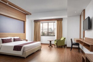 Una habitación de hotel con cama, escritorio, silla, televisión y ventana con cortinas.
