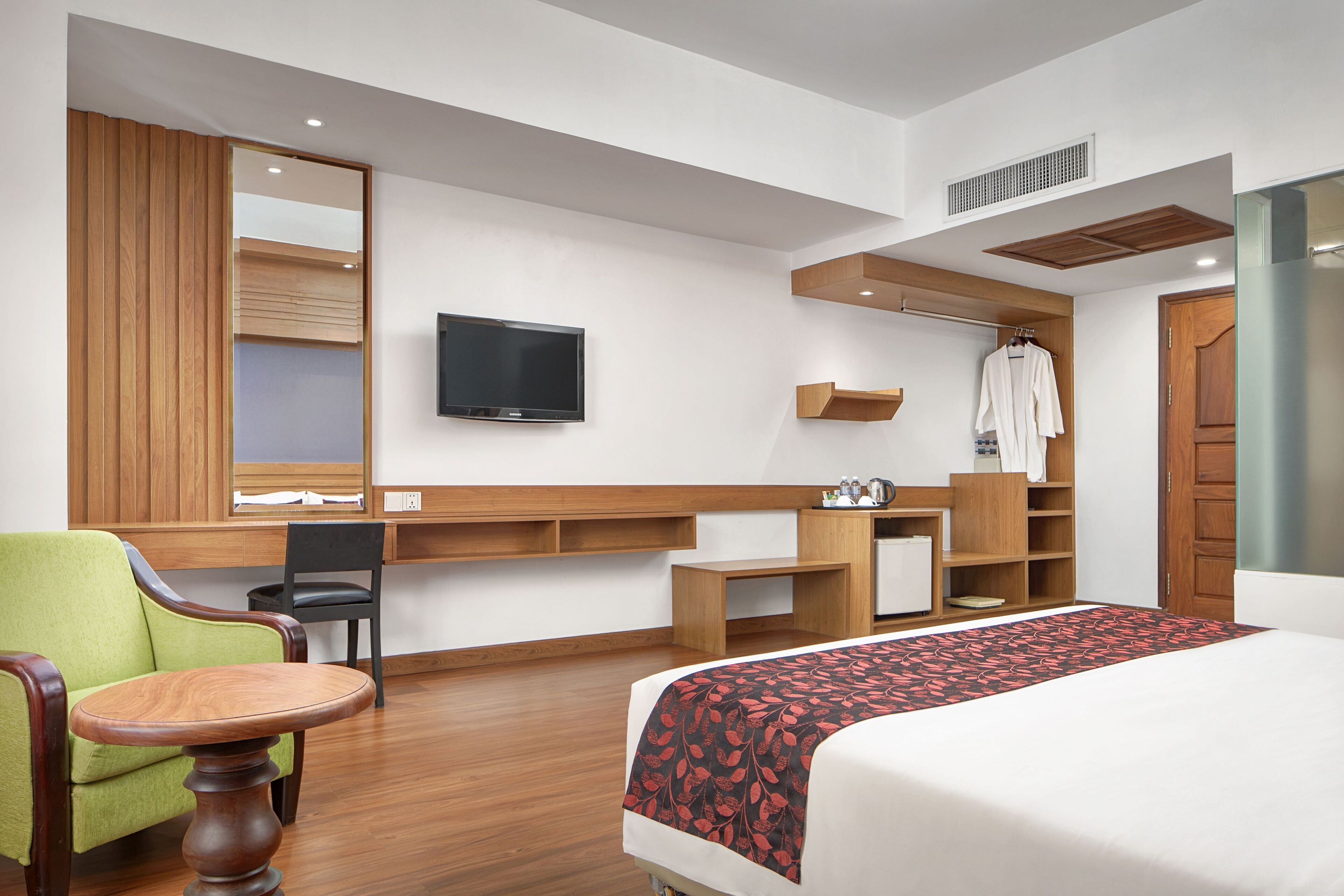 Una habitación de hotel con una cama, un sillón verde, un escritorio de madera, un televisor y un armario.