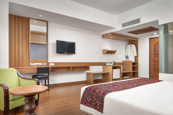A hotel room with a bed, a green armchair, a wooden desk, a television, and a wardrobe. - Ohana Phnom Penh Palace Hotel (Phnom Penh)