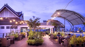 Un bar situé sur le toit, avec une terrasse, une vue sur la ville et un espace couvert agrémenté de guirlandes lumineuses.