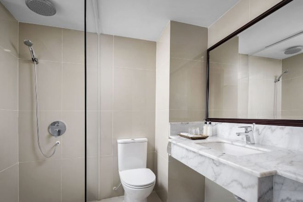A modern bathroom with a shower, toilet, and a marble sink with a mirror.