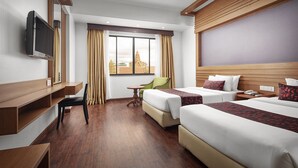 Une chambre d’hôtel avec deux lits, un bureau, une chaise, une télévision et une fenêtre avec des rideaux.