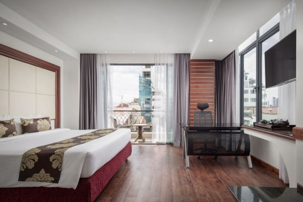 A hotel room with a large bed, a desk, and a view of a cityscape.