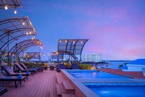 A rooftop pool area with lounge chairs and umbrellas, overlooking a body of water and city skyline. - Ohana Phnom Penh Palace Hotel (Phnom Penh)