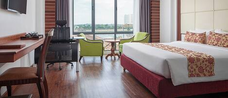 Ein Hotelzimmer mit einem großen Bett, einem Schreibtisch mit Stuhl, einem kleinen Tisch und einem an der Wand befestigten Fernseher.