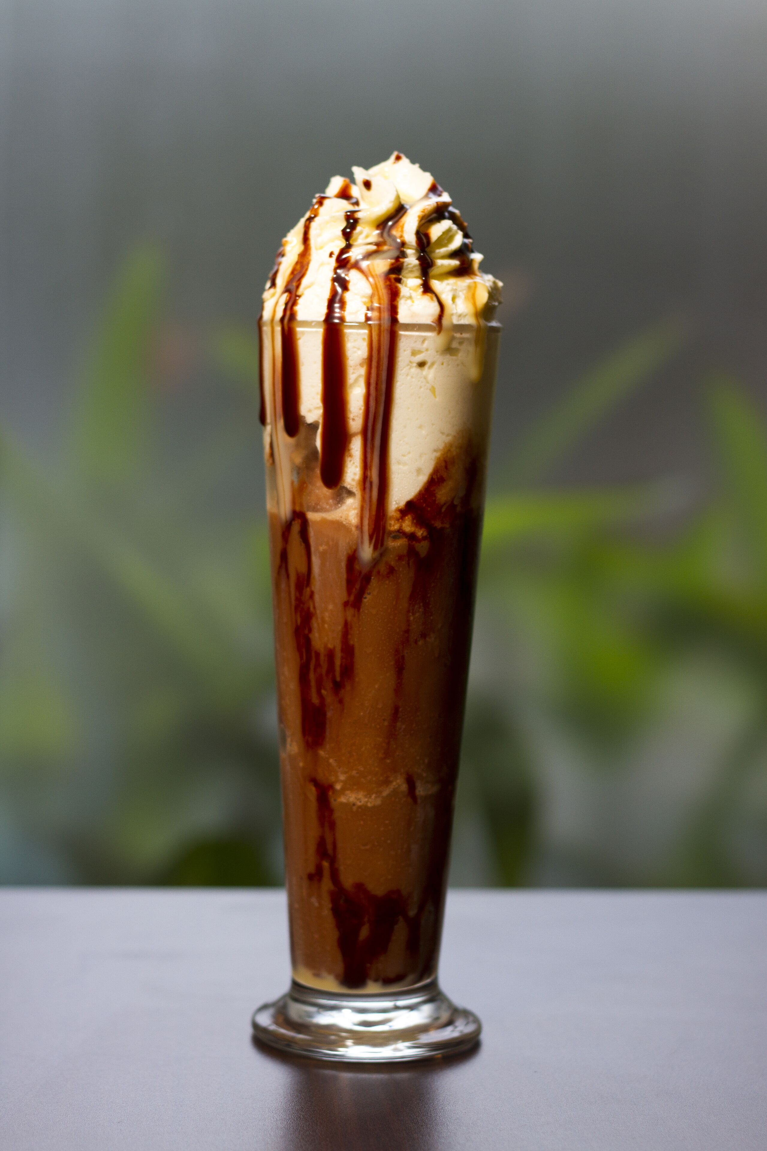 Un grand verre rempli d’un dessert à la crème fouettée et nappé de sauce au chocolat.