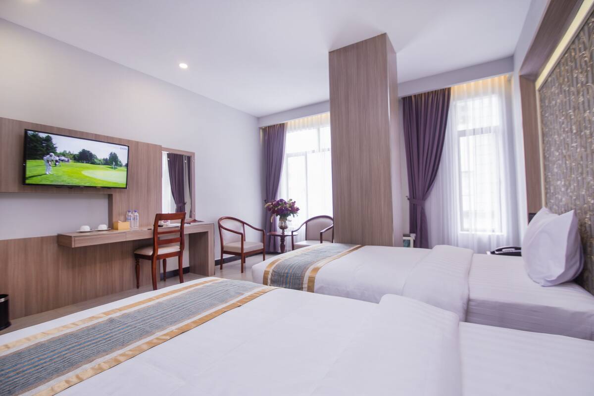 A hotel room with two beds, a desk, a TV, and a window with curtains.