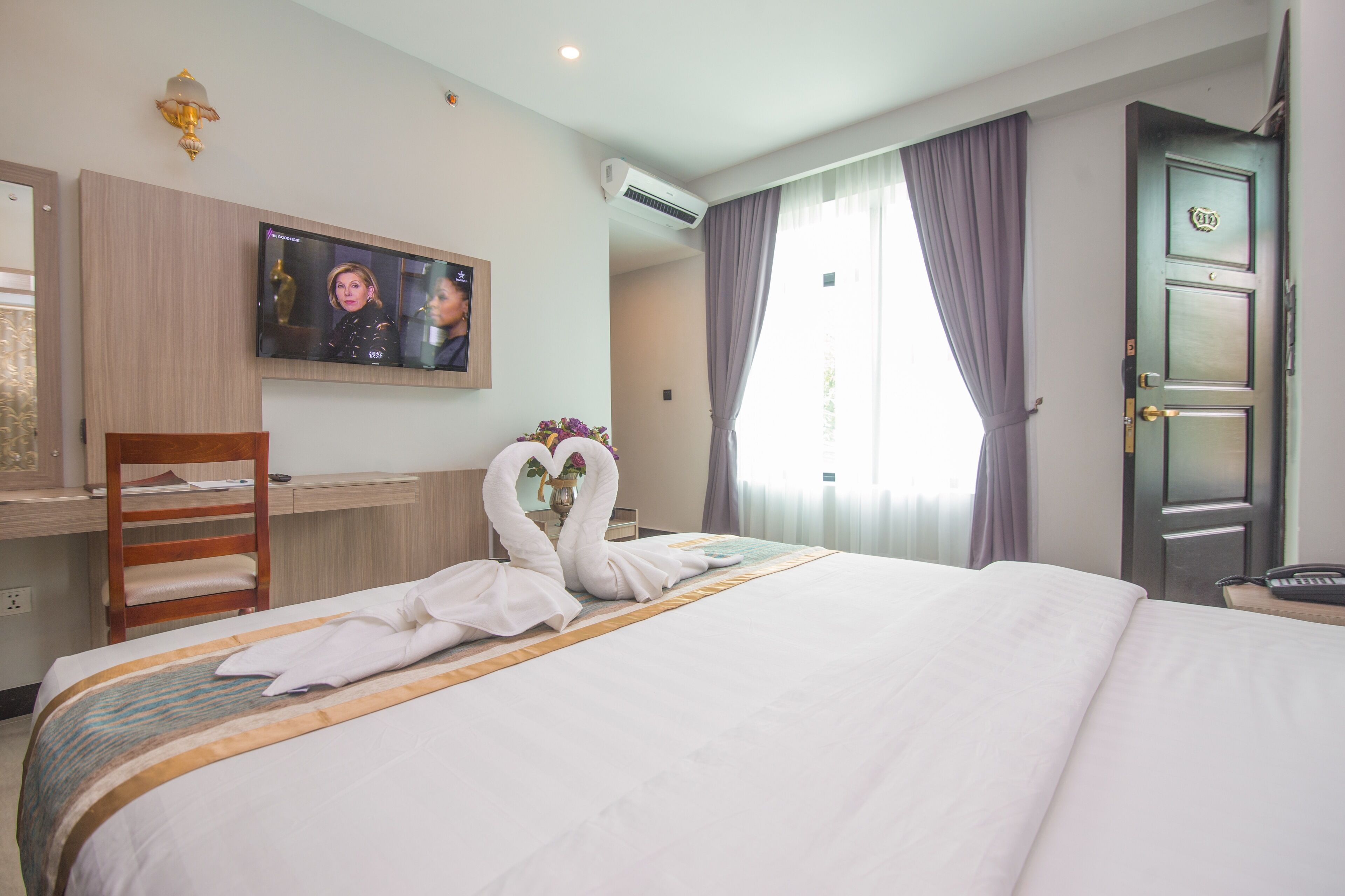 Ein Hotelzimmer mit einem großen Bett, einem Schreibtisch mit Stuhl, einem an der Wand montierten Fernseher und einer Tür mit Griff.