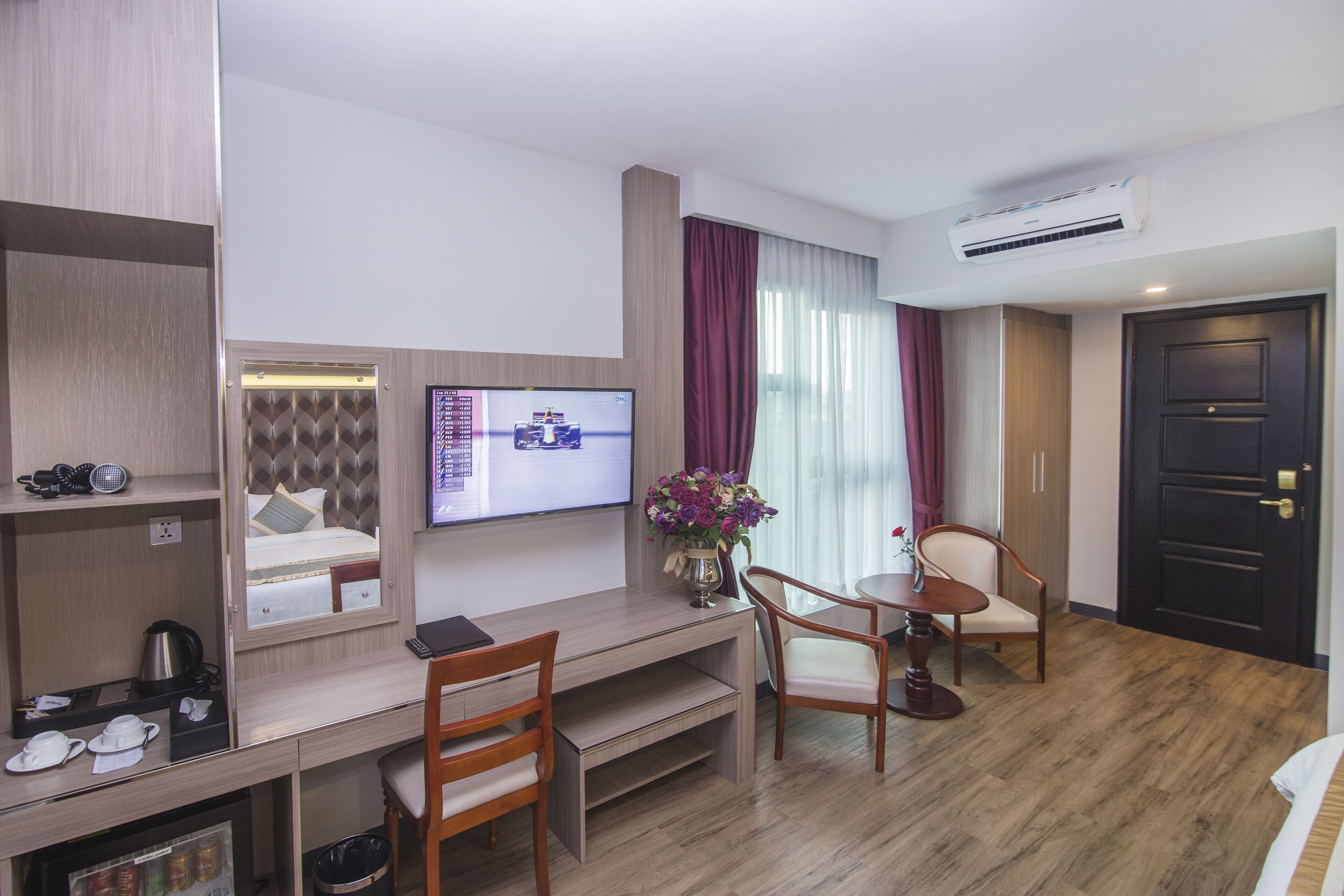 Ein Hotelzimmer mit Bett, Schreibtisch mit Computer, Stuhl, Fernseher und einem Fenster mit Vorhängen.