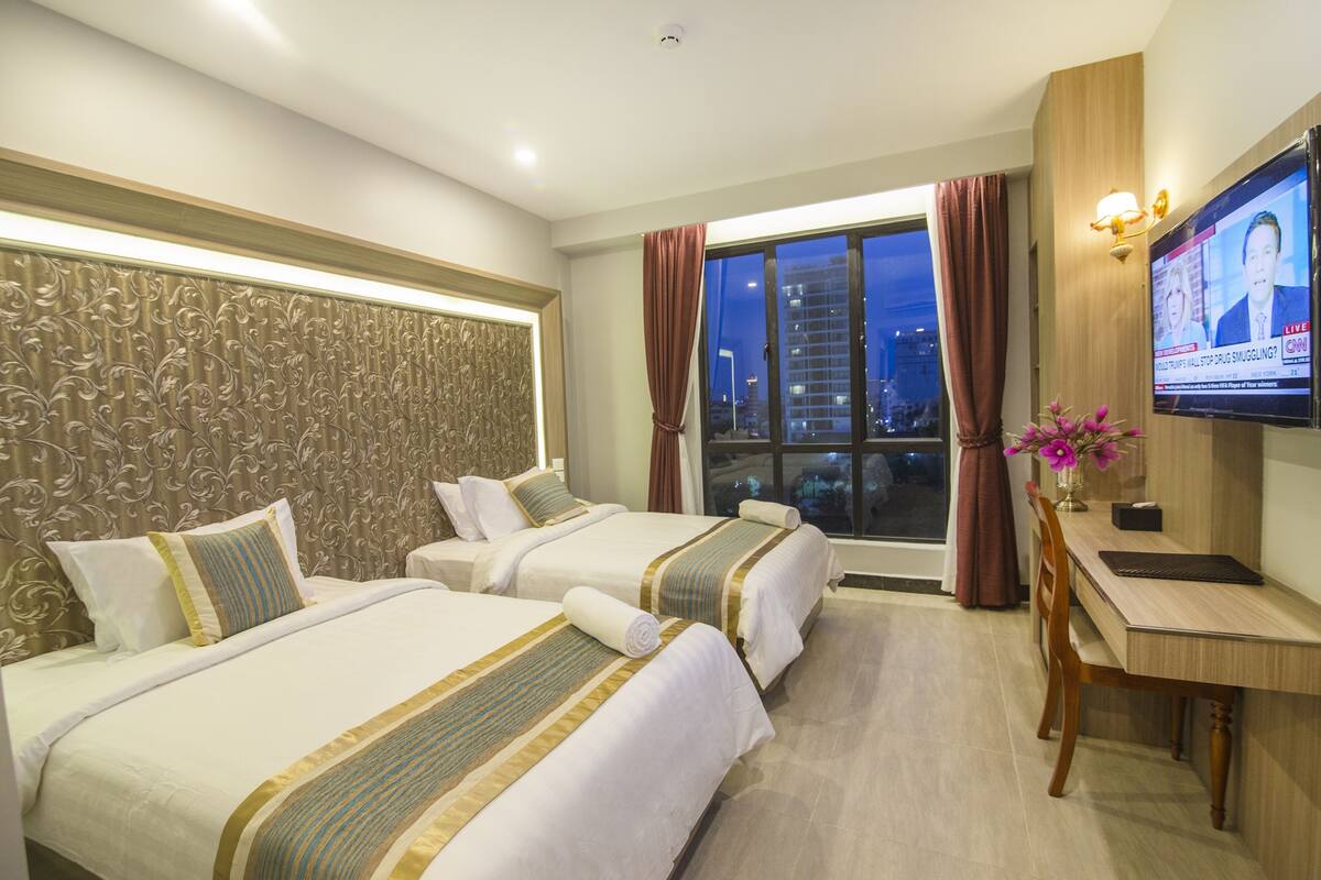 A hotel room with two beds, a desk, a TV, and a window with curtains.