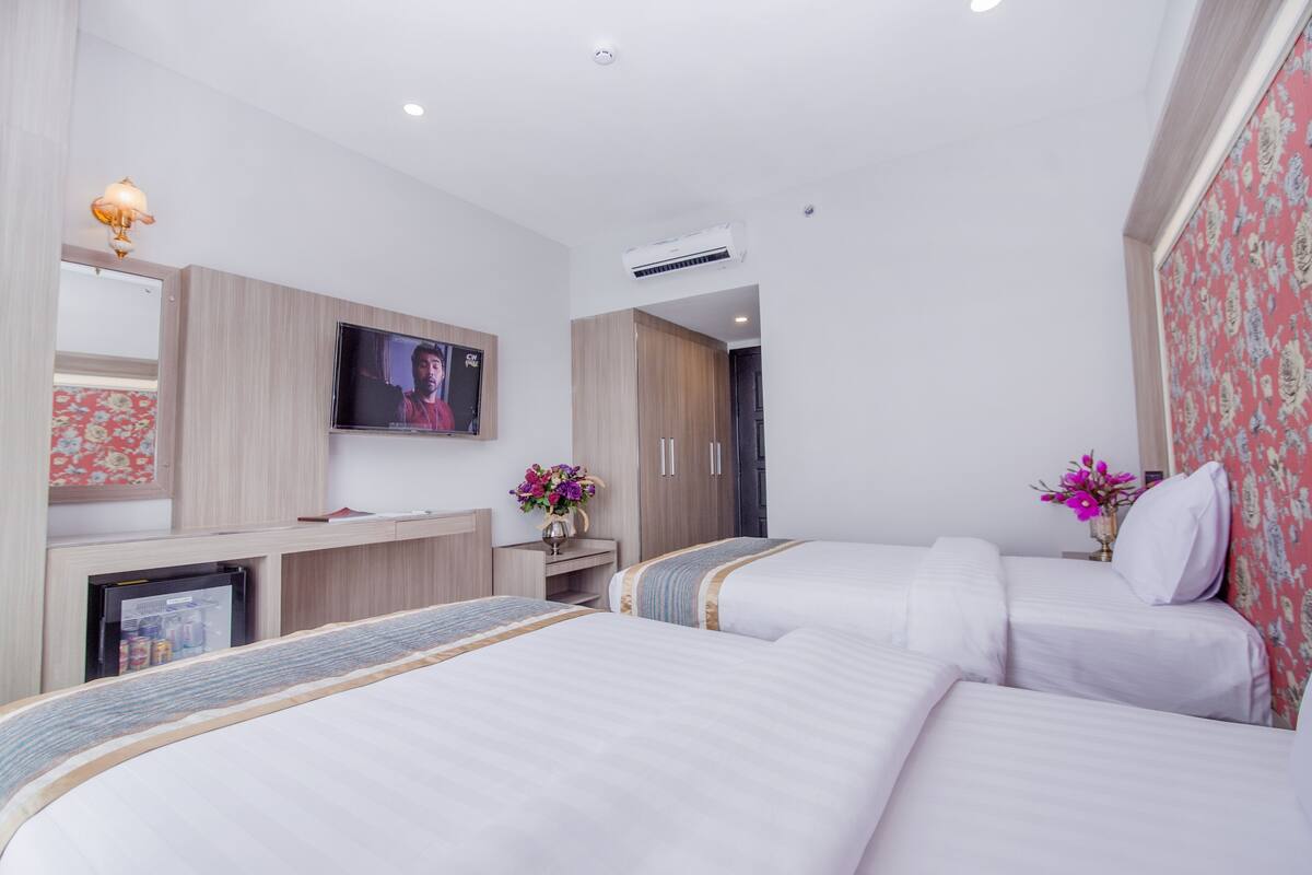 A hotel room with two beds, a TV, a desk, and a refrigerator.