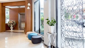 A modern lobby with a large window, a potted plant, and a decorative metal partition. - New York Hotel (Phnom Penh)