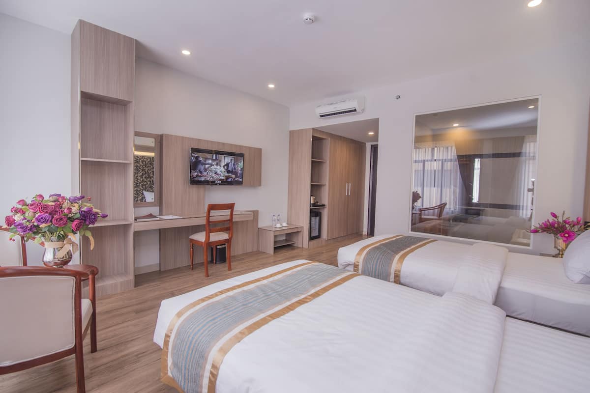 A hotel room with two beds, a desk, a chair, a TV, and a bathroom visible through a glass door.