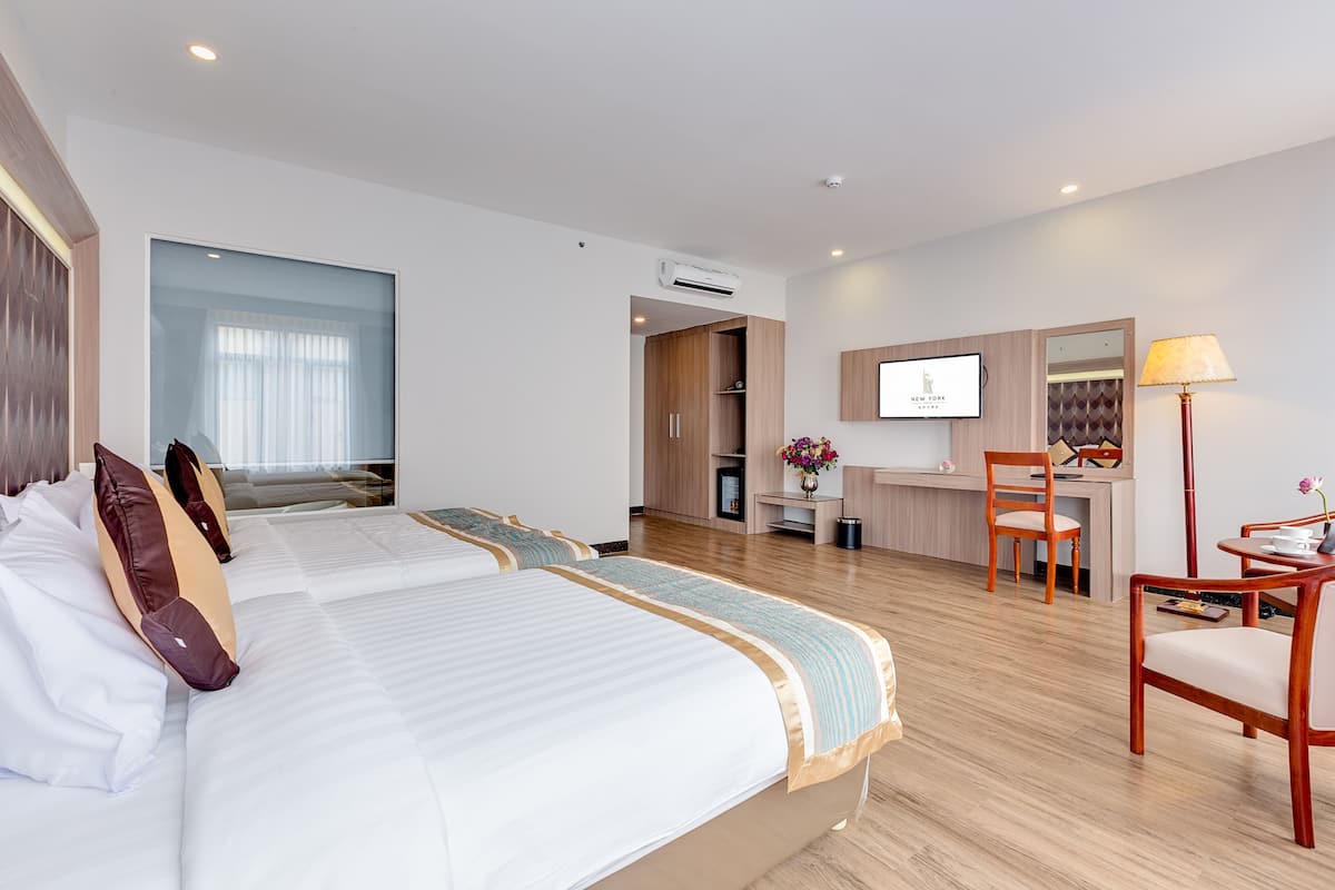 A hotel room with two beds, a desk, a chair, and a TV.