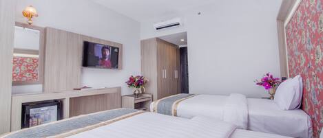 A hotel room with two beds, a TV, a minibar, and a desk with a lamp.