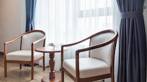 A room with two wooden chairs and a small round table, a window with sheer curtains, and a view of the city. - New York Hotel (Phnom Penh)