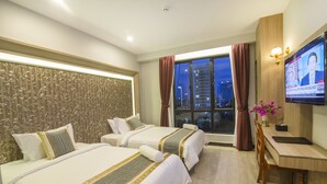 A hotel room with two beds, a desk, a TV, and a window with curtains. - New York Hotel (Phnom Penh)