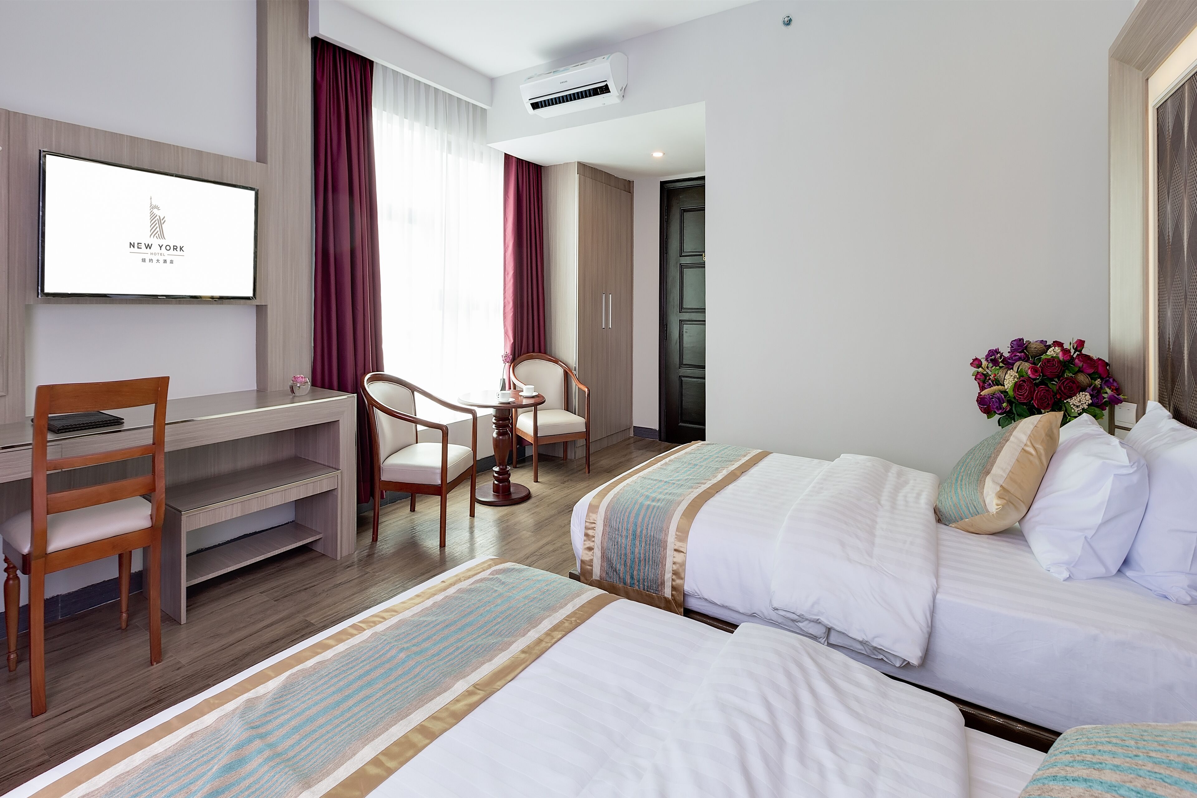 Habitación de hotel con dos camas, un escritorio, una silla, un televisor y una ventana con cortinas.