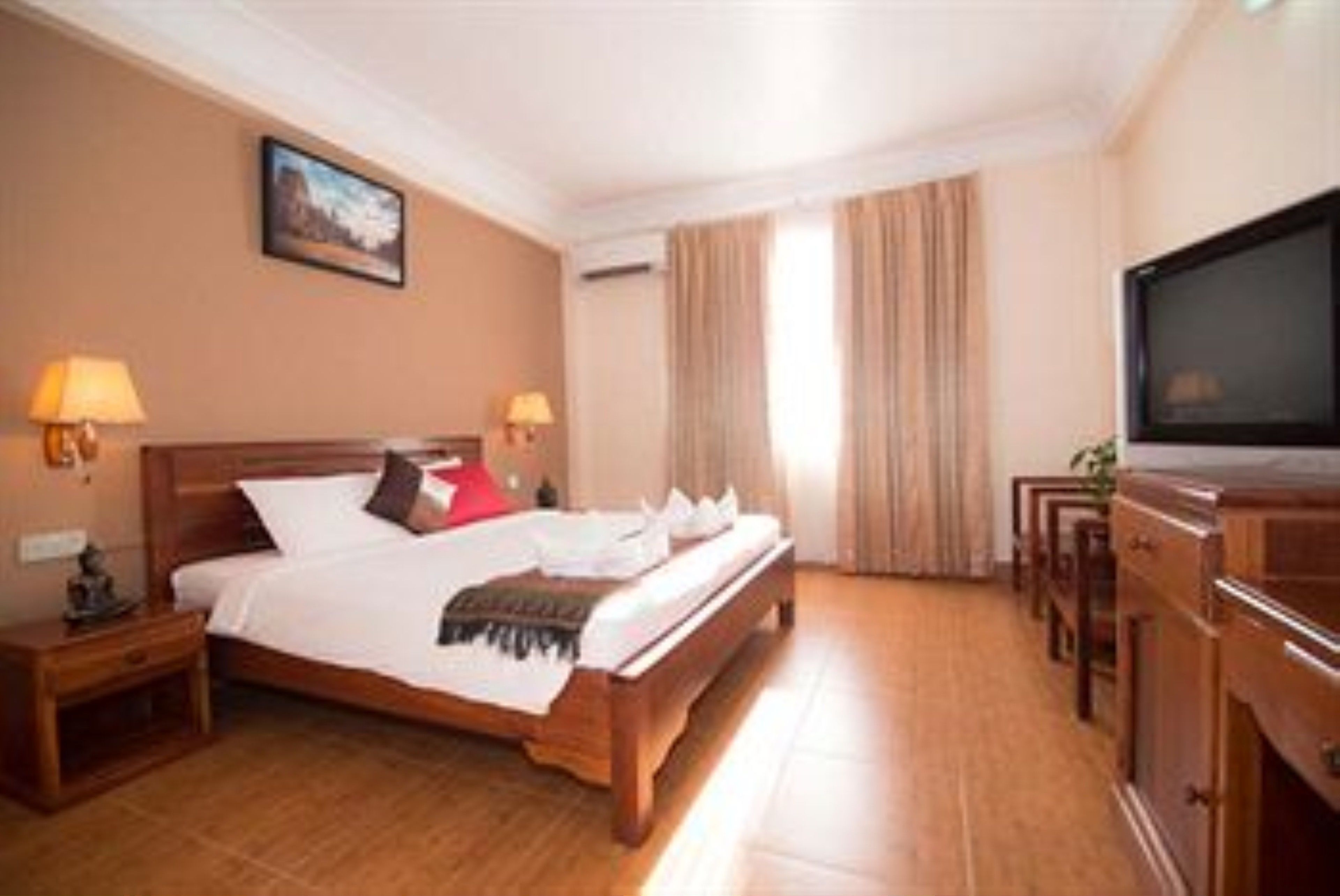 A hotel room with a wooden bed, two bedside tables with lamps, a television, and a large window with curtains.