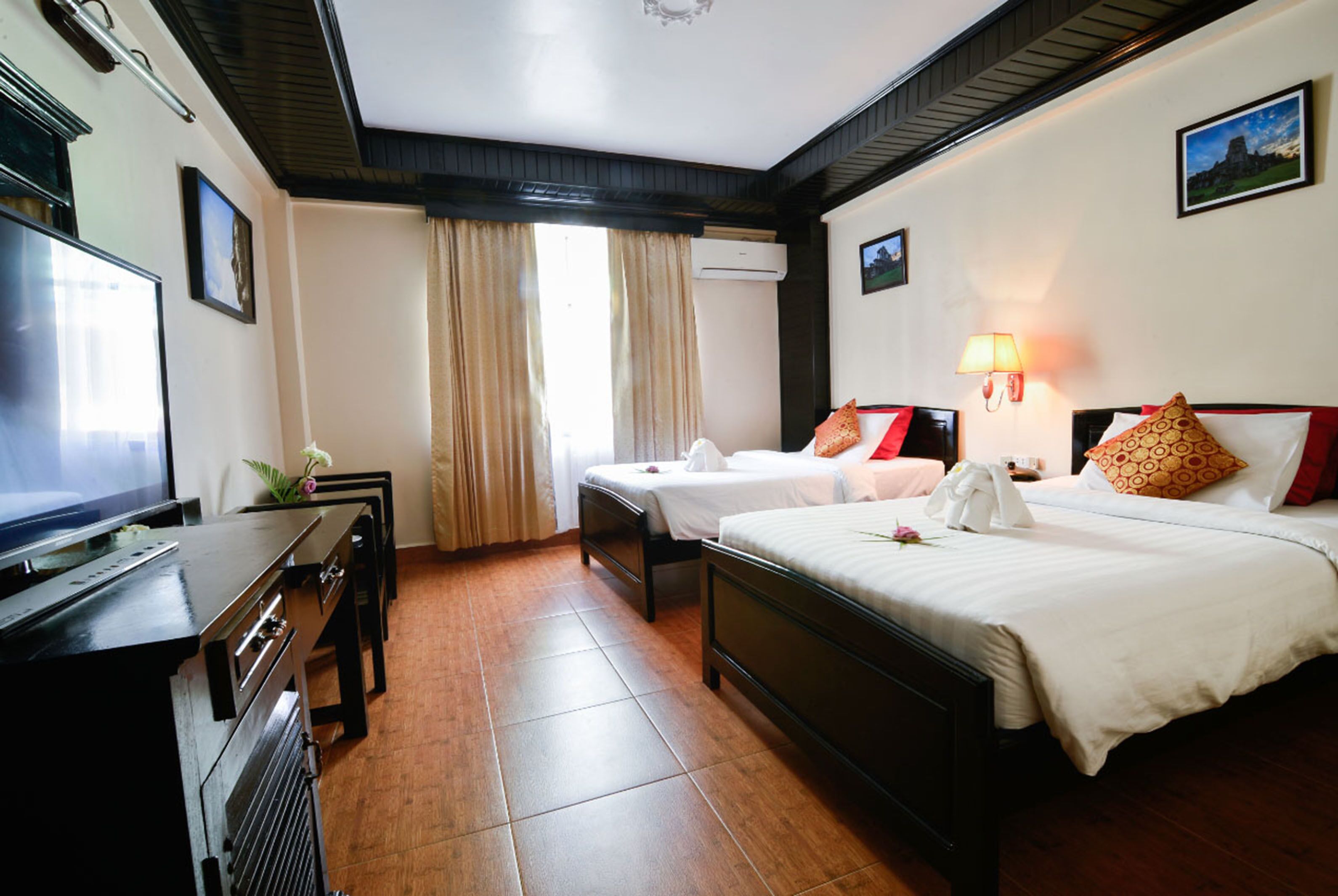 A hotel room with a TV, two beds, a desk, and a lamp.