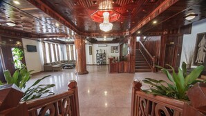 A spacious lobby with a polished floor, wooden railings, a staircase, and a large chandelier.