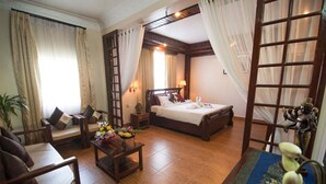 A hotel room with a bed, two chairs, a small table with flowers, and a decorative mirror.