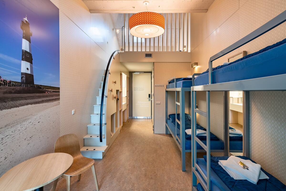 Une chambre avec des lits superposés, une petite table et une chaise. Un escalier mène à une autre pièce.