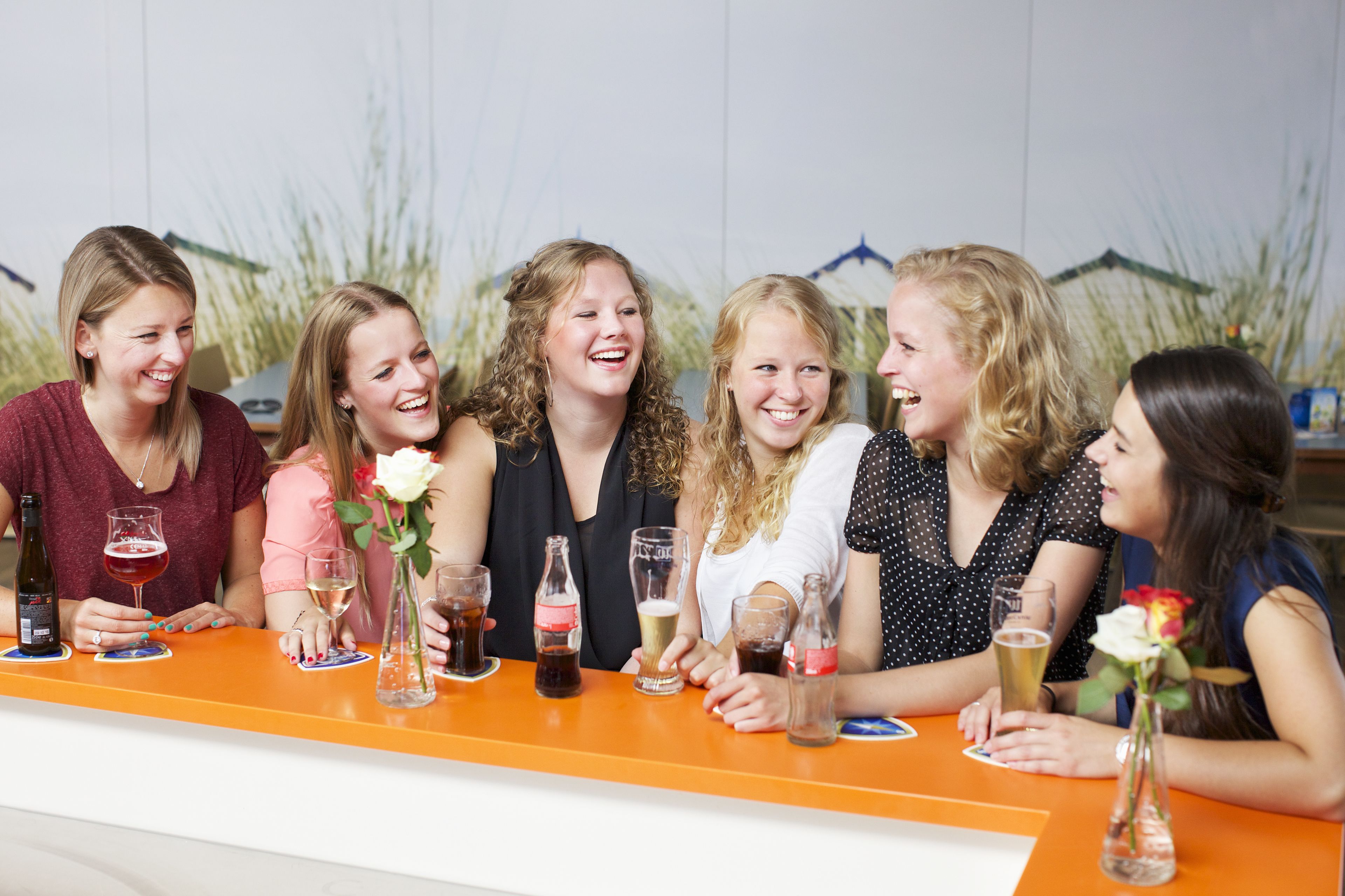 A group of people seated at a bar with various drinks and a vase of flowers.