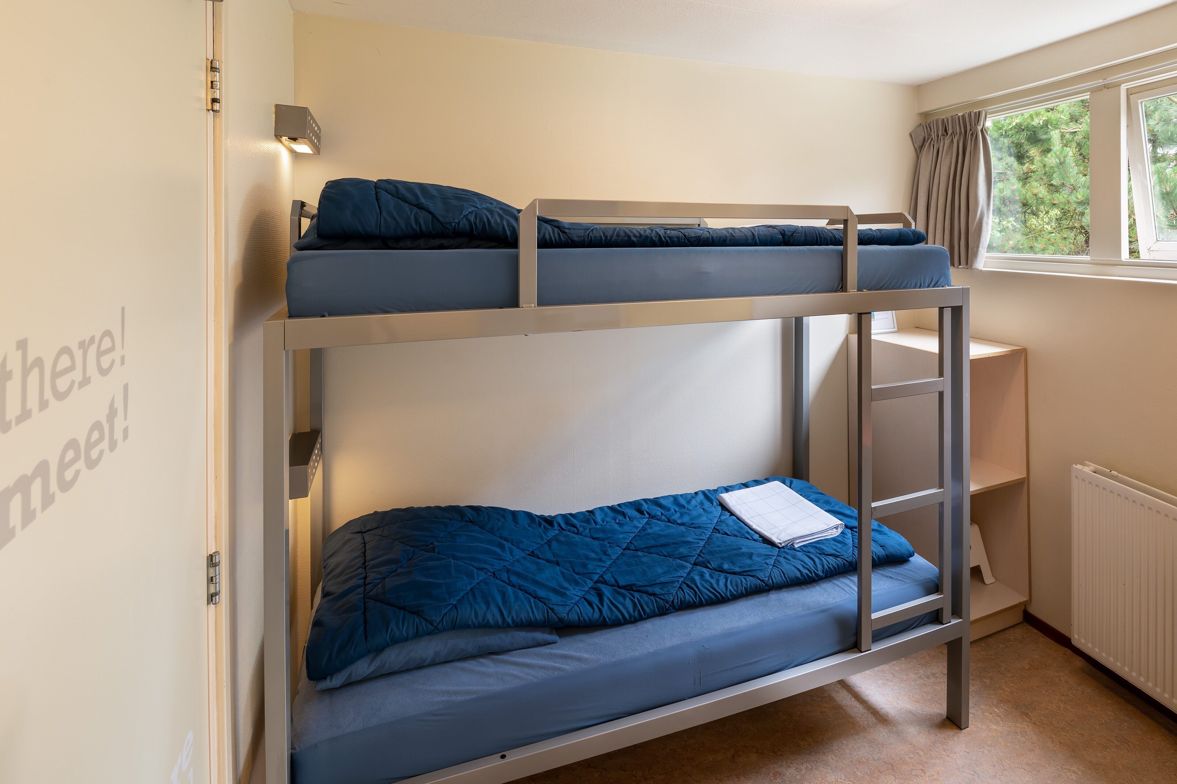 A bunk bed room with a window, a radiator, and a shelf.