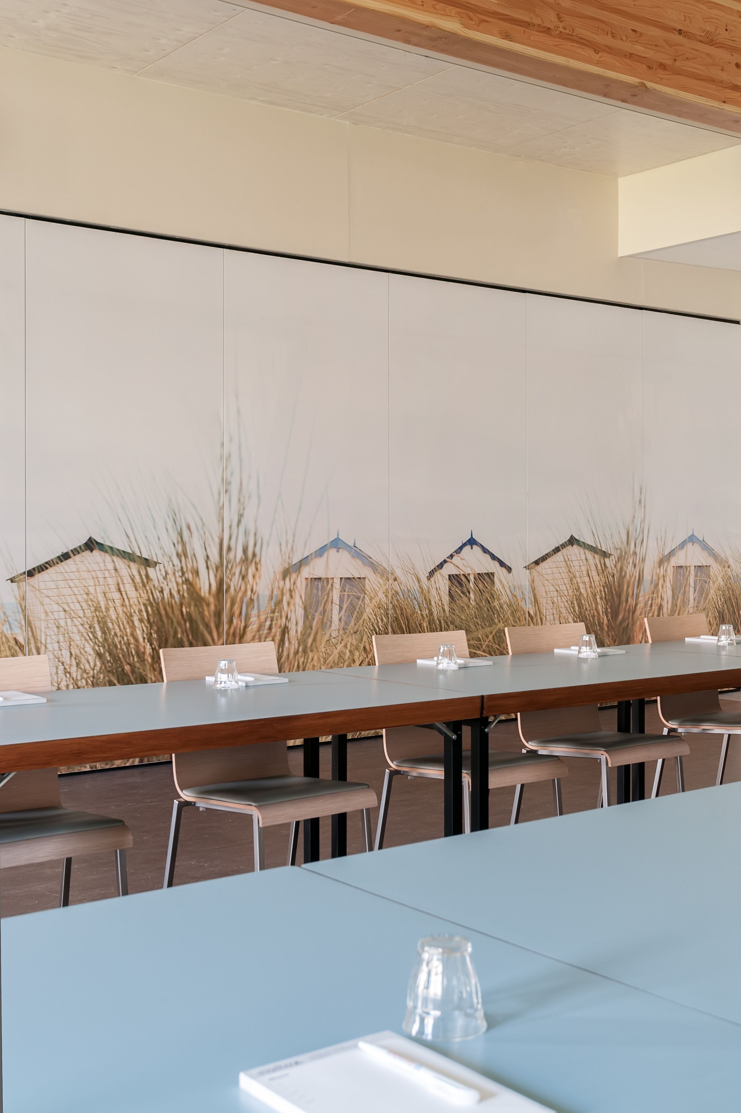 A conference room with a long table, chairs, and a backdrop of tall grasses and house silhouettes.