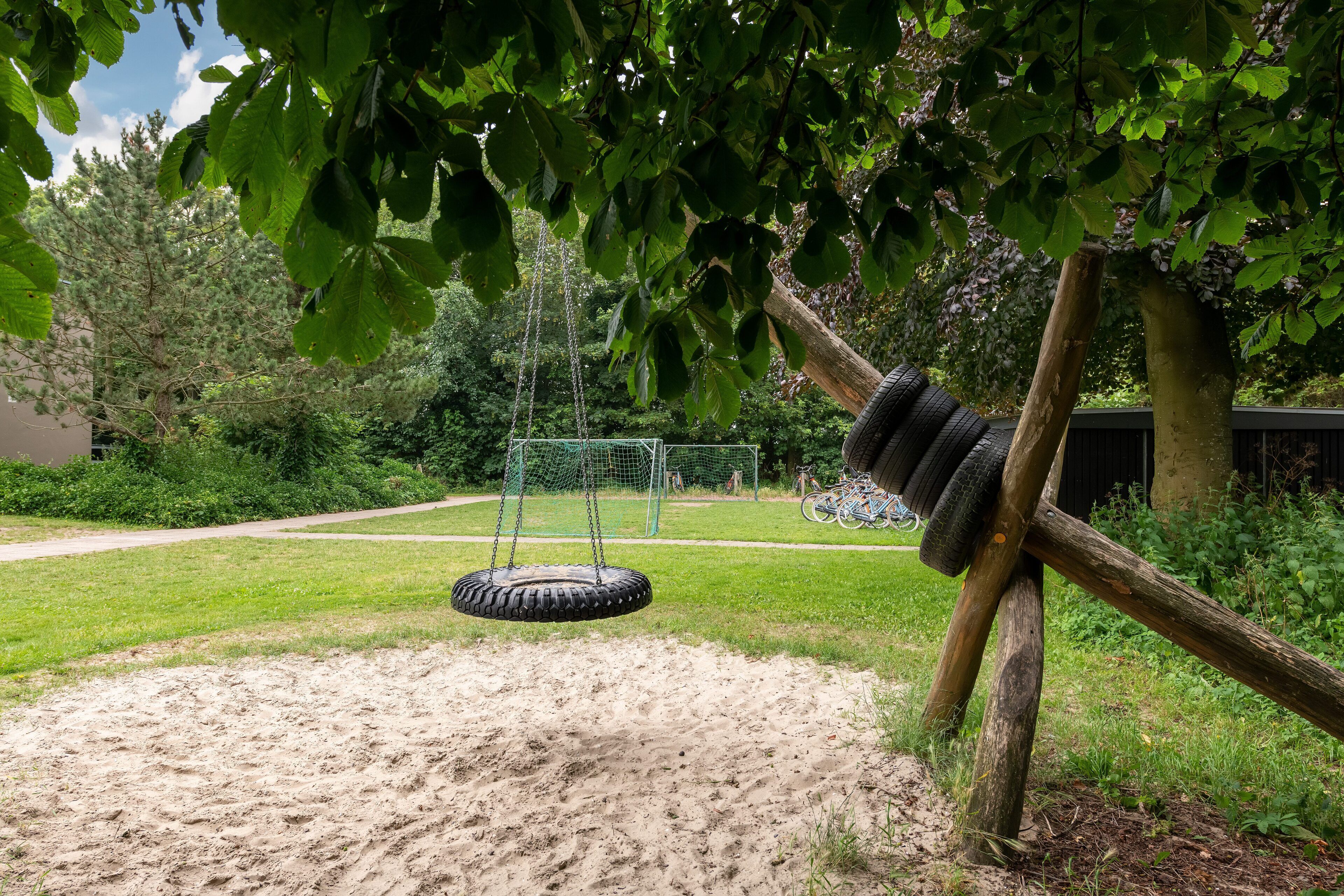 A playground with a tire swing, a tire swing hanging from a tree, and a soccer goal.
