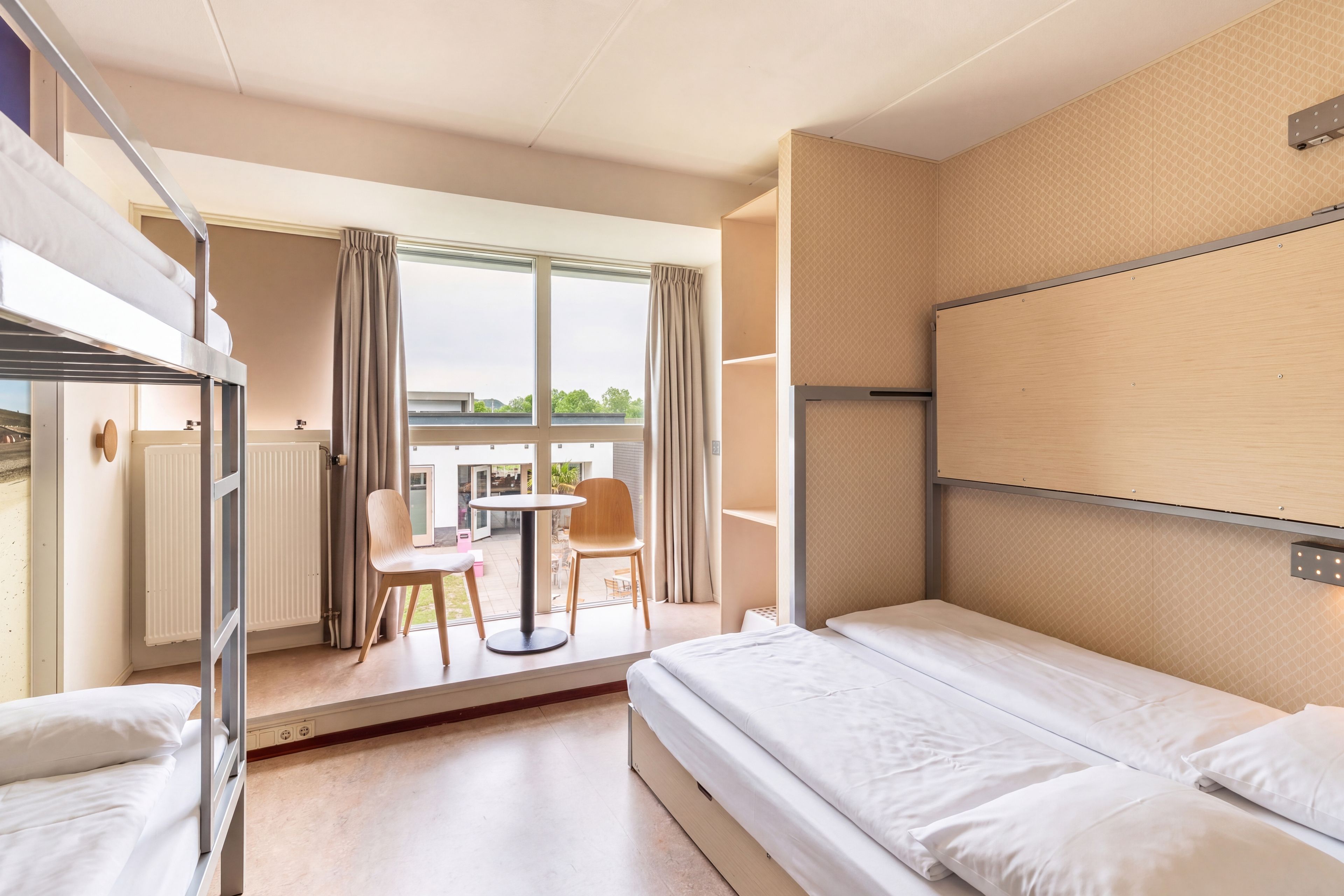 Une chambre d’hôtel avec un lit superposé, une petite table avec des chaises et une vue sur l’extérieur.