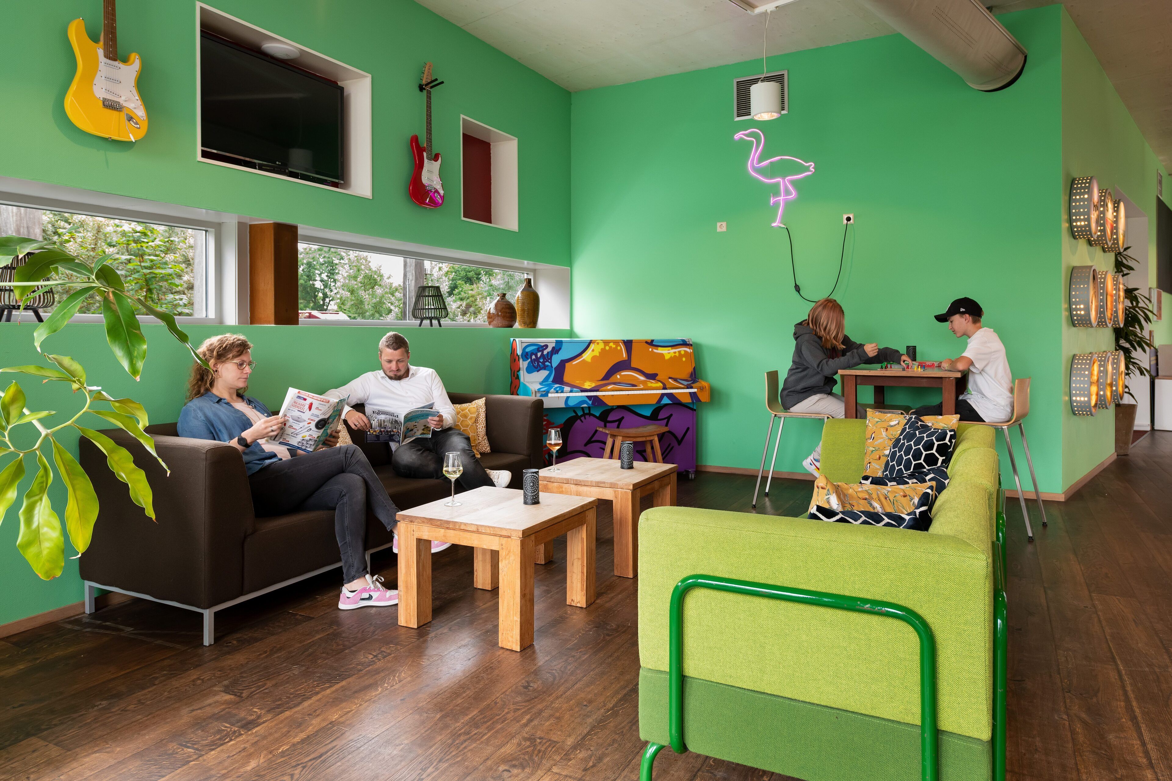 Una habitación vibrante con paredes verdes, muebles de madera y una silla verde. Hay guitarras en la pared, un cuadro y un letrero de neón.