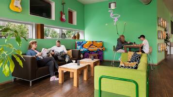 Una habitación vibrante con paredes verdes, muebles de madera y una silla verde. Hay guitarras en la pared, un cuadro y un letrero de neón.