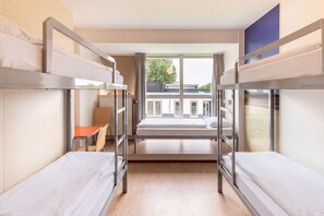 Une chambre de dortoir avec des lits superposés, une petite table et une fenêtre donnant sur les bâtiments environnants.