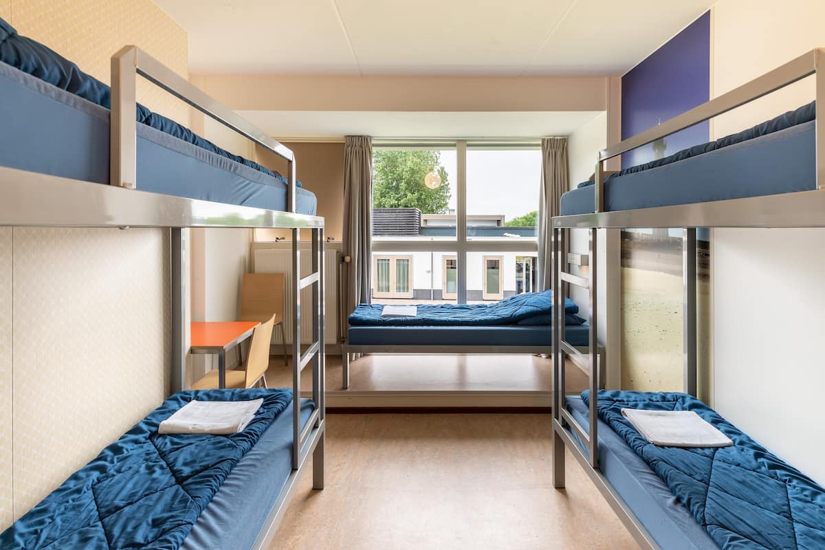 Une chambre de dortoir avec des lits superposés, une petite table et une vue sur l’extérieur.