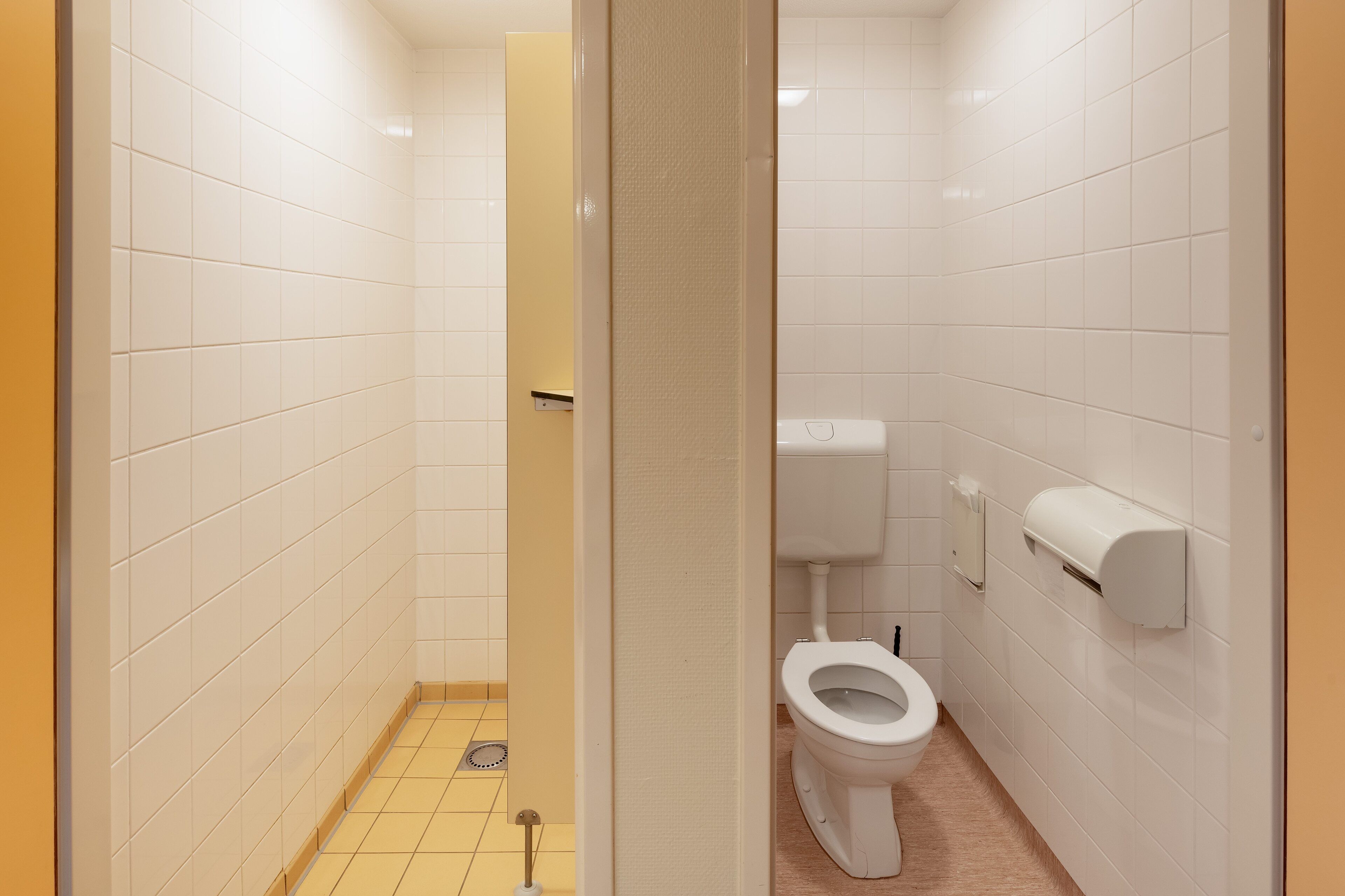 Un baño pequeño y limpio con azulejos blancos, un inodoro y un dispensador de toallas de papel.