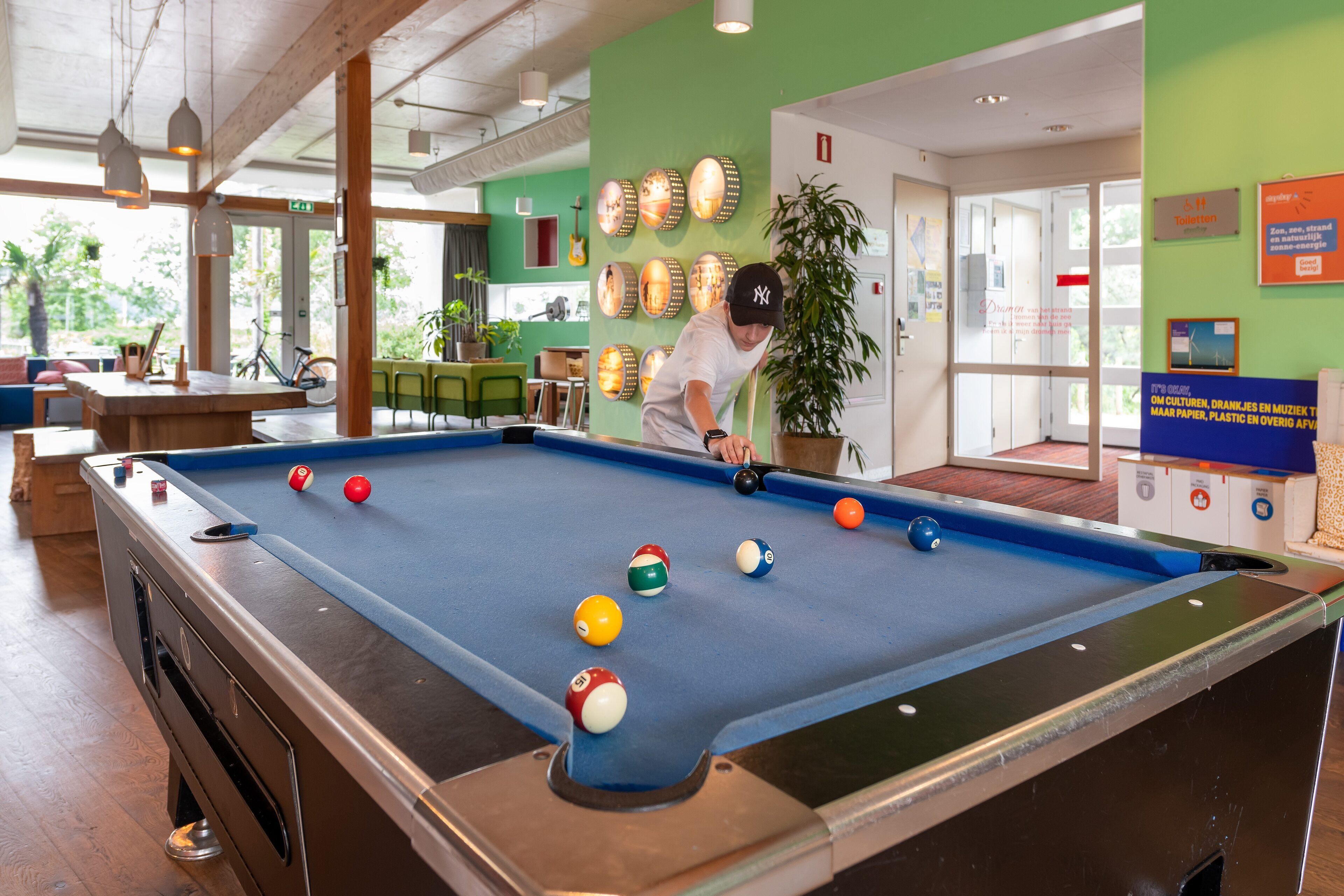 A pool table with balls, a person playing, and a green wall with various decorations.
