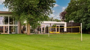 Un bâtiment moderne doté d’une façade en verre, d’une terrasse et d’un filet de volley-ball.