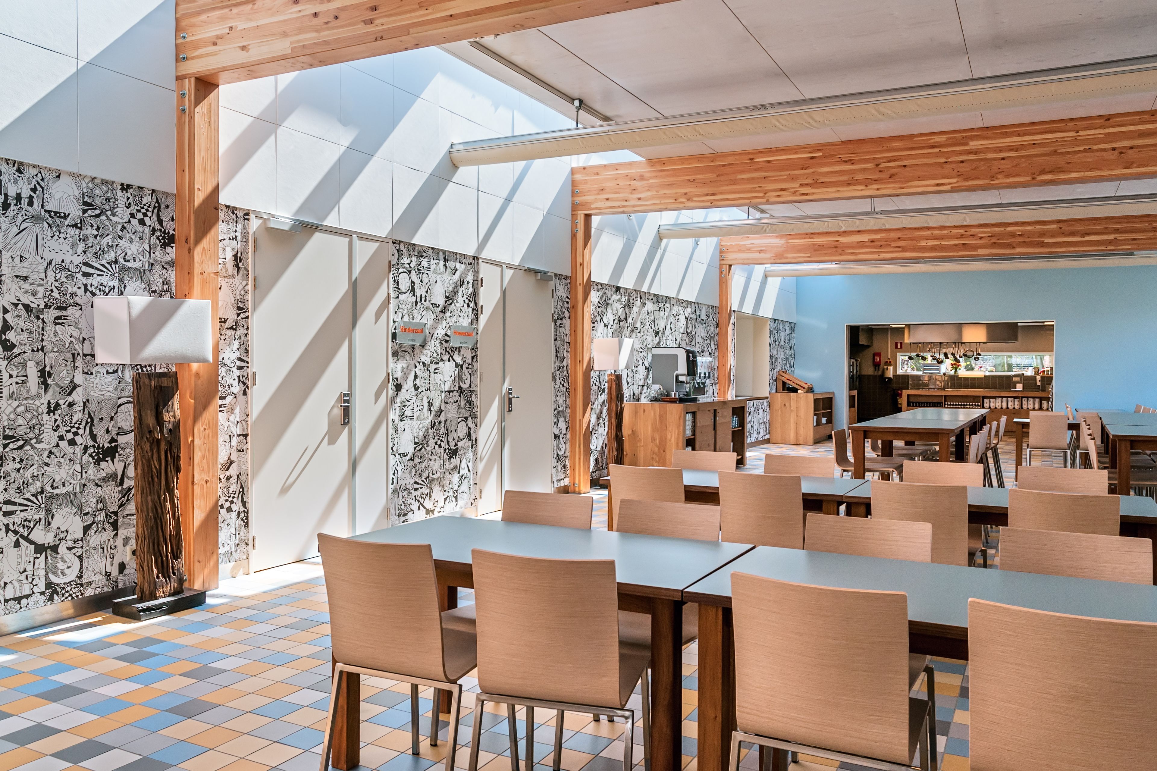 Un comedor moderno con mesas y sillas de madera, una cocina al fondo y paredes con diseño.
