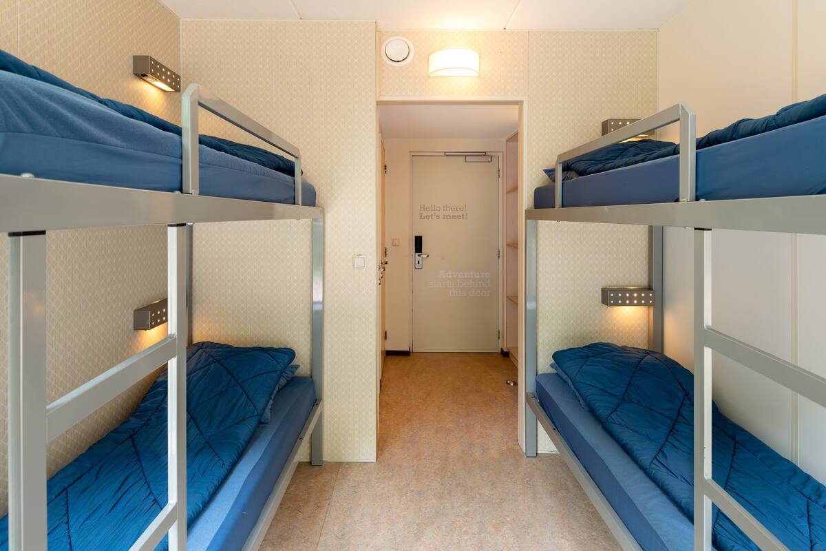Une chambre avec deux lits superposés, une porte avec une pancarte et un luminaire au-dessus de la porte.
