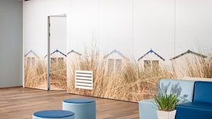 Un intérieur moderne avec un plancher en bois, un canapé bleu, une table basse en bois et un mur orné d’une fresque représentant un paysage de plage.