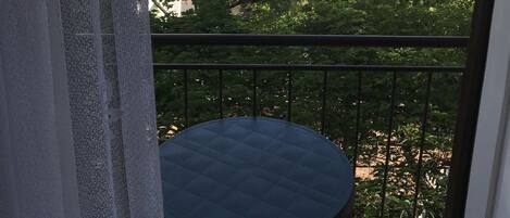 Un balcon avec une table ronde, donnant sur une zone côtière avec des bâtiments et des arbres.