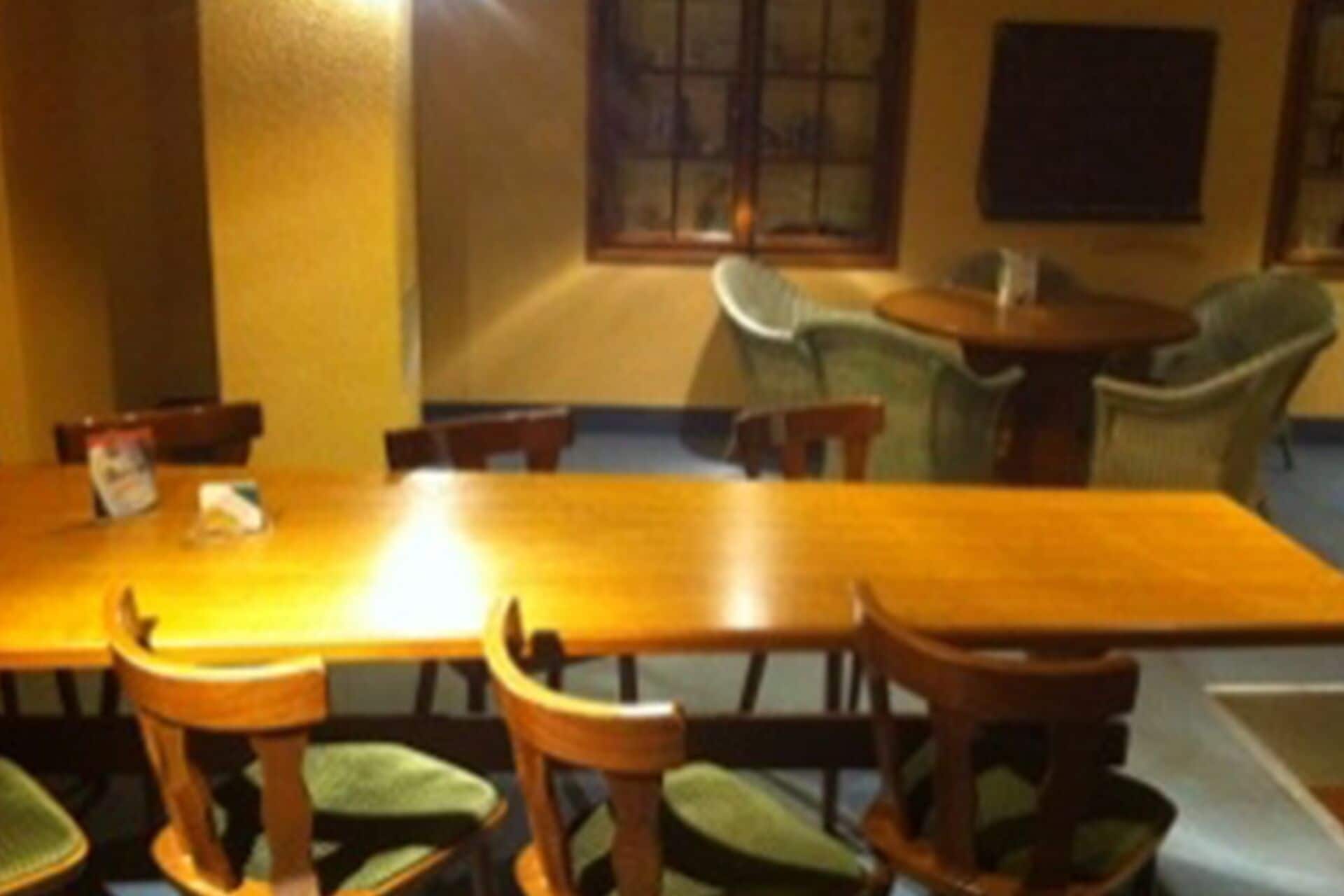 A dining area with a long wooden table, several chairs, and a window with blinds.