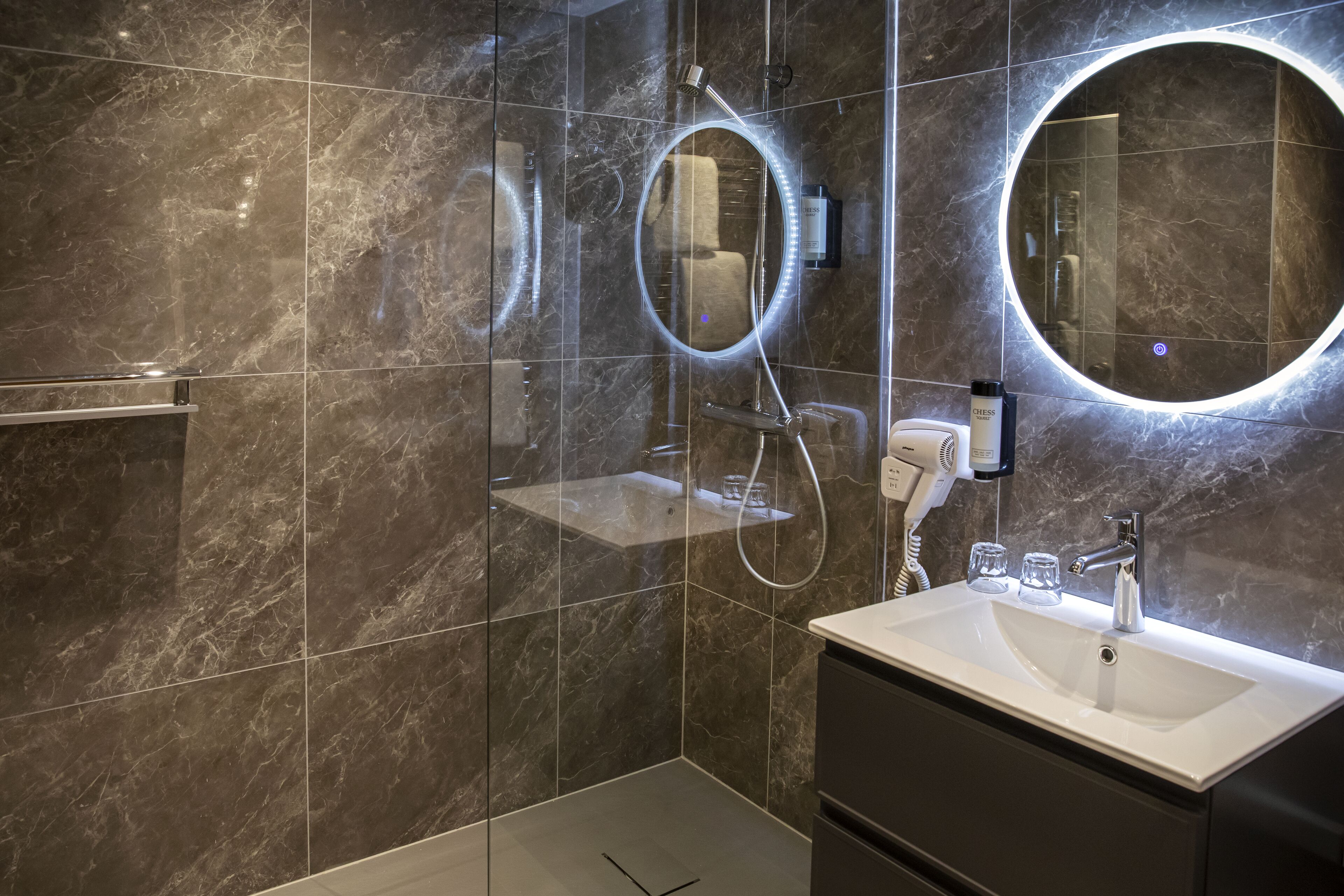 Een moderne badkamer met een douchebekleding van marmer, een wastafelmeubel en twee ronde spiegels.