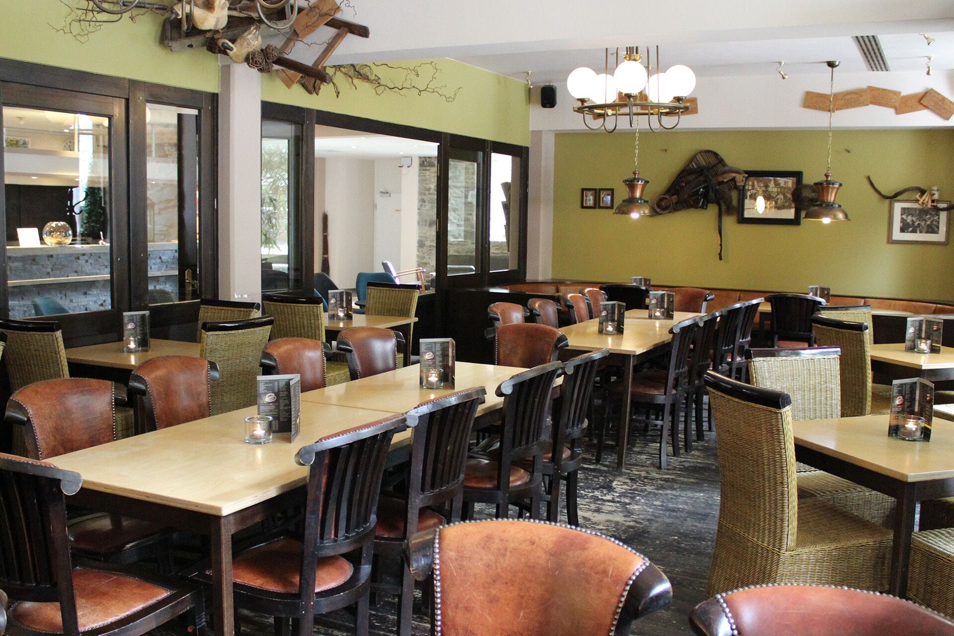A restaurant with wooden tables and leather chairs, large windows, and a chandelier.
