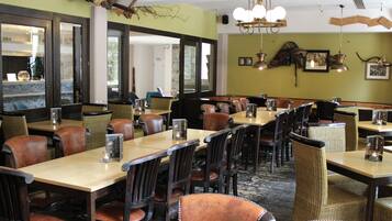 A restaurant with wooden tables and leather chairs, large windows, and a chandelier.