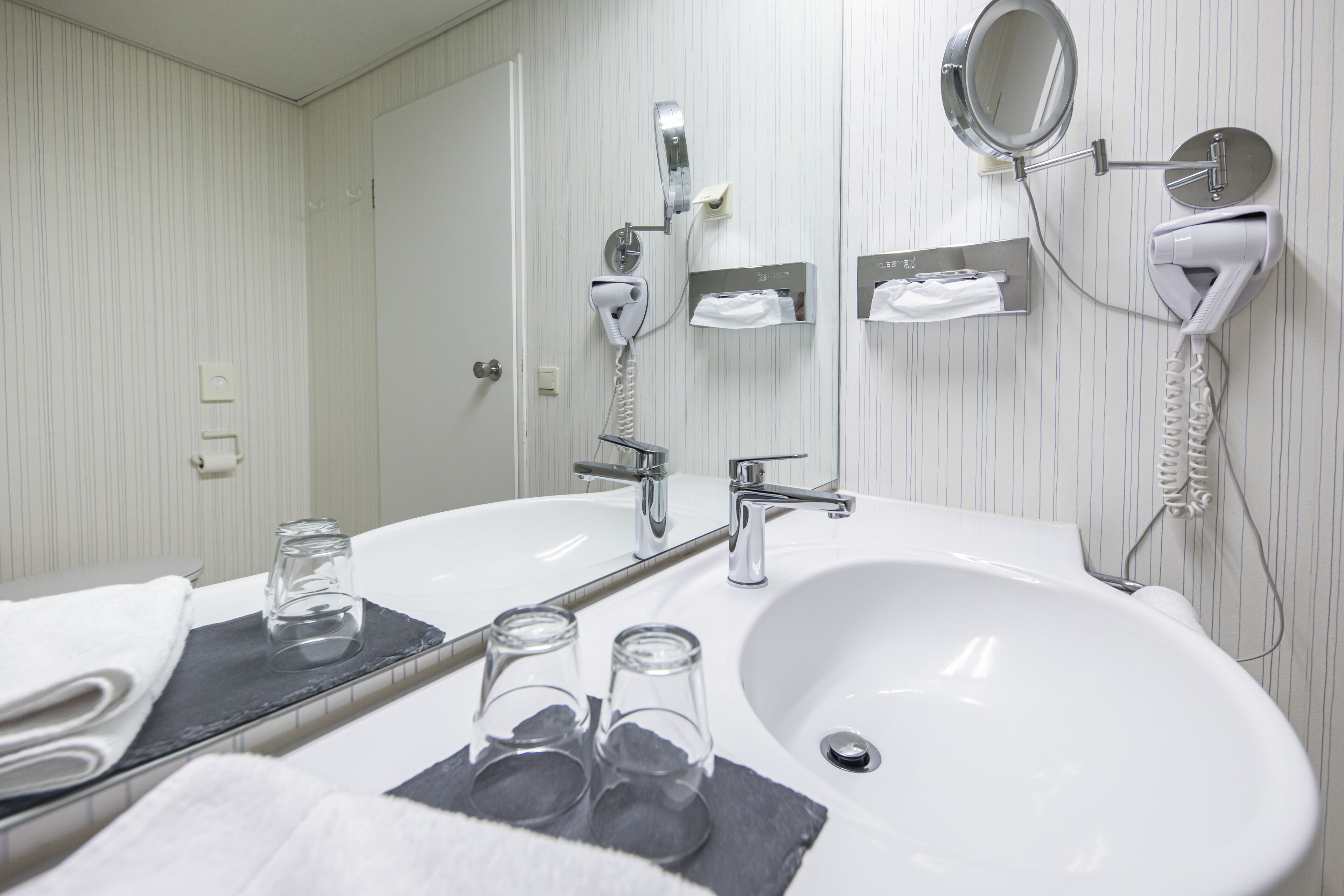 Une salle de bain moderne avec un grand lavabo, un miroir, un sèche-cheveux et un porte-serviettes.
