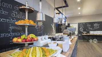 Un bufé de desayuno con diversas frutas y bebidas, una pizarra con texto e iluminación moderna.