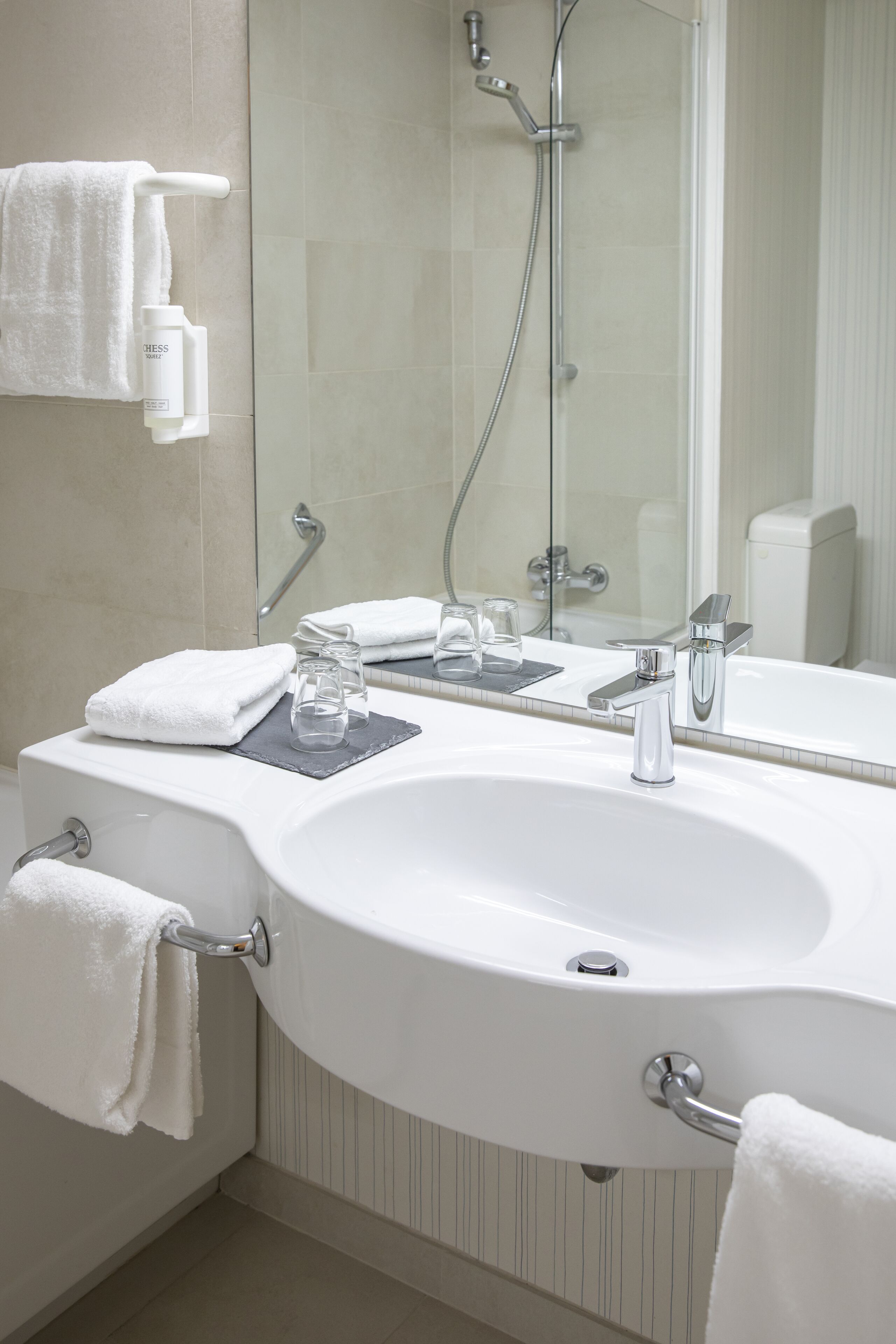 Un baño moderno con un lavamanos blanco, dos llaves, ducha de vidrio y un espejo.